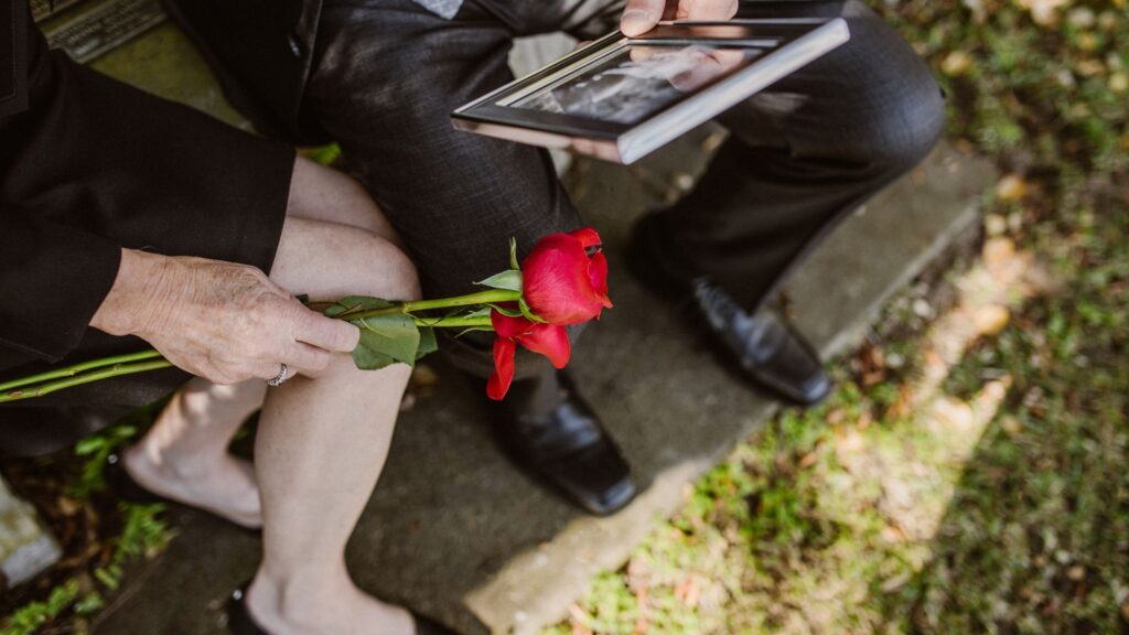 Man and woman dressed in black, grieving a wrongful death, with rose and picture frame in hand.