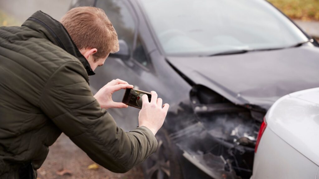 Man taking pictures of damage to his car after an accident.