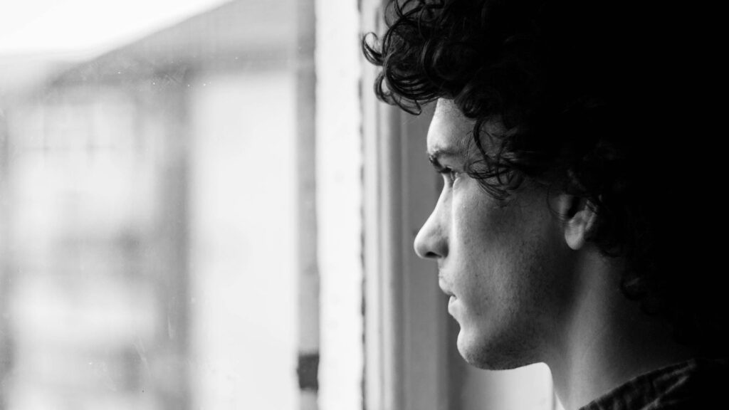 Black and grey image of a pensive man gazing out a window.