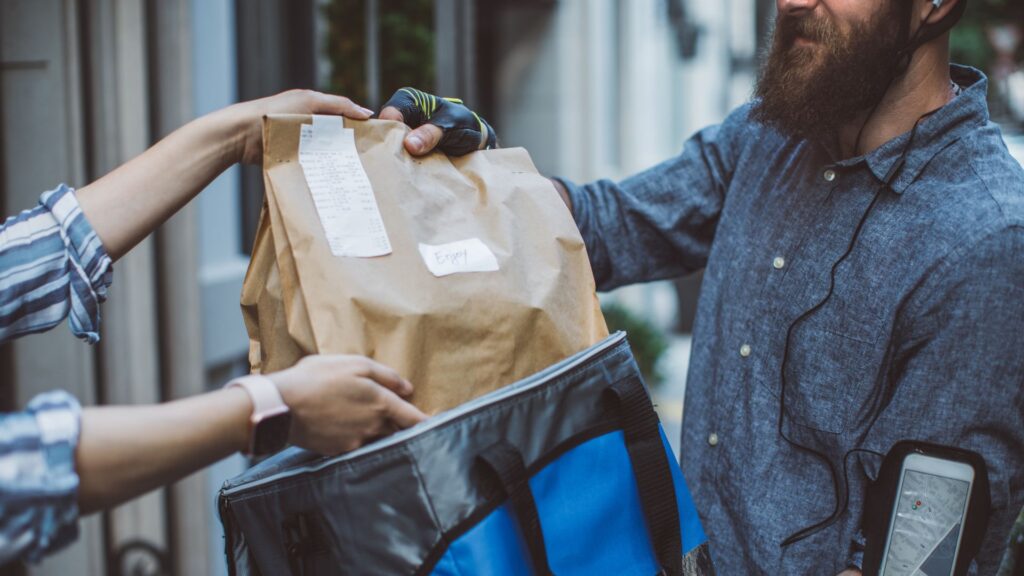A food delivery man handing a customer's food bag to her.