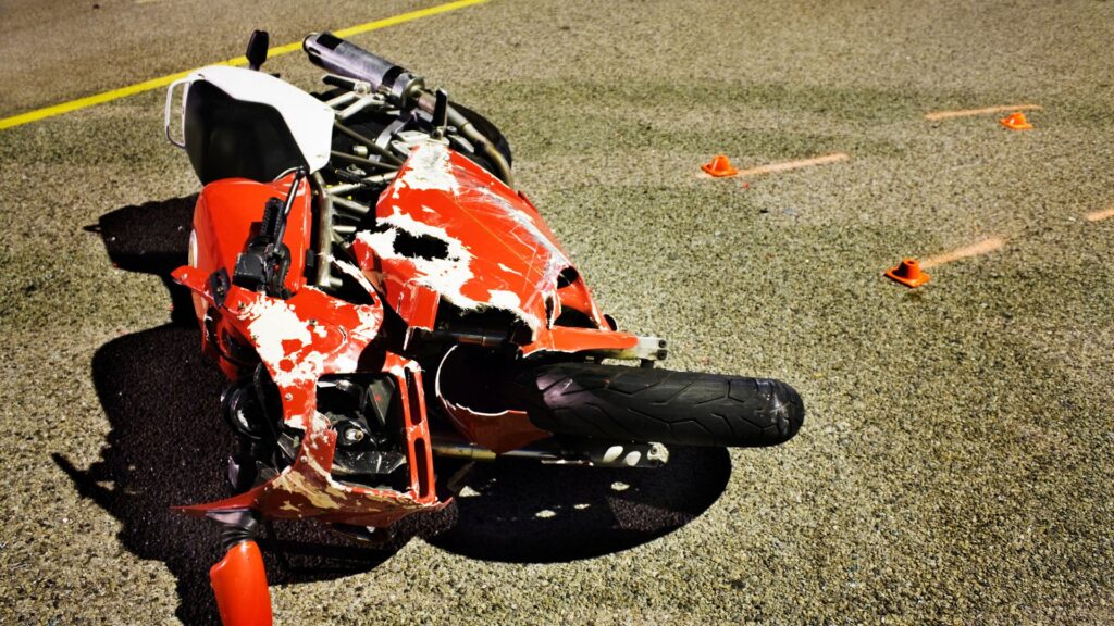 Red motorcycle toppled over at the scene of an accident with orange evidence markers by its side.