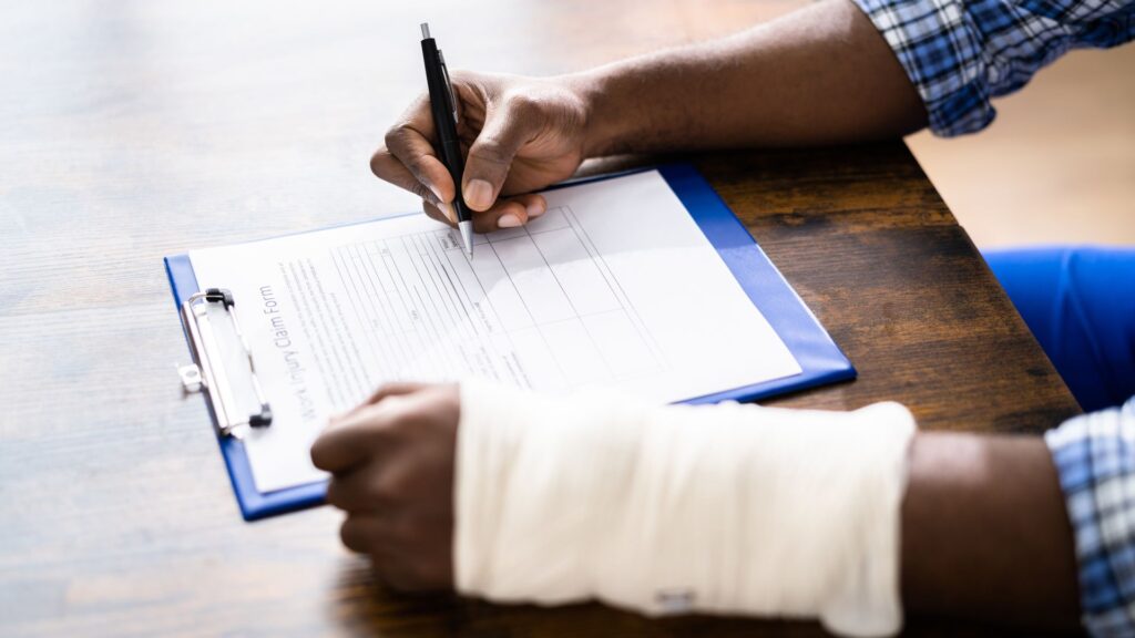 Man with a cast on his arm signing a form to claim his personal injury damages.