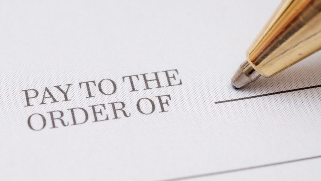 The "pay to the order of" section of a check with a pen about to write on it.