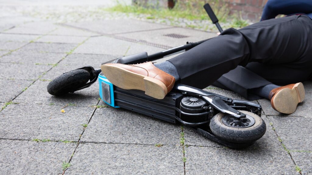 Man in business attire and his electric scooter on the ground after suffering a scooter accident.