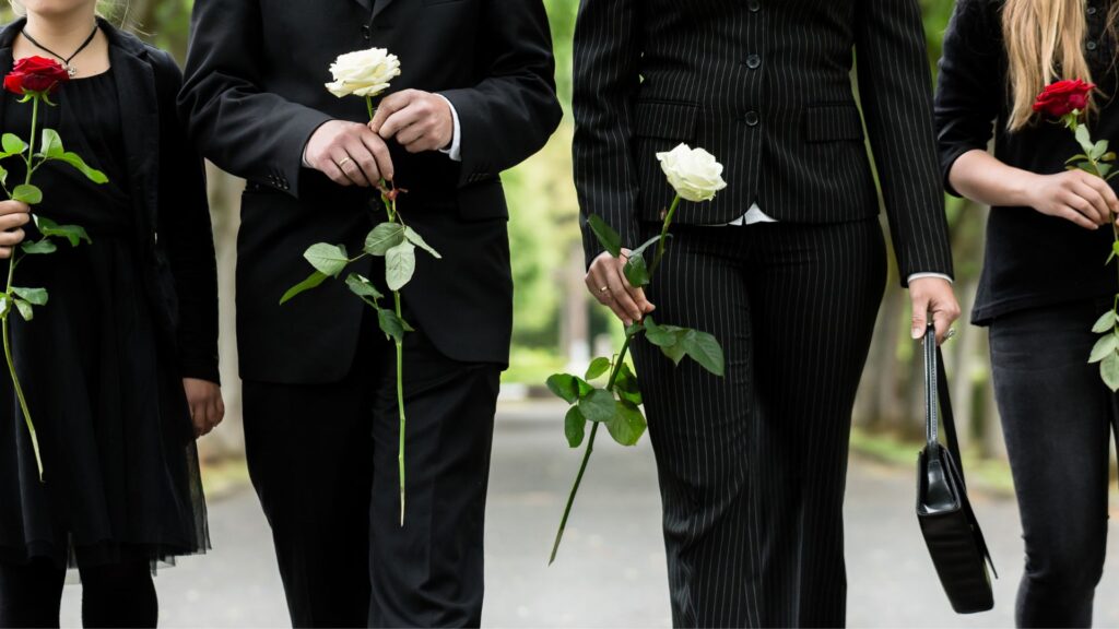 A grieving family of four dressed in black walking side by side and carrying roses.