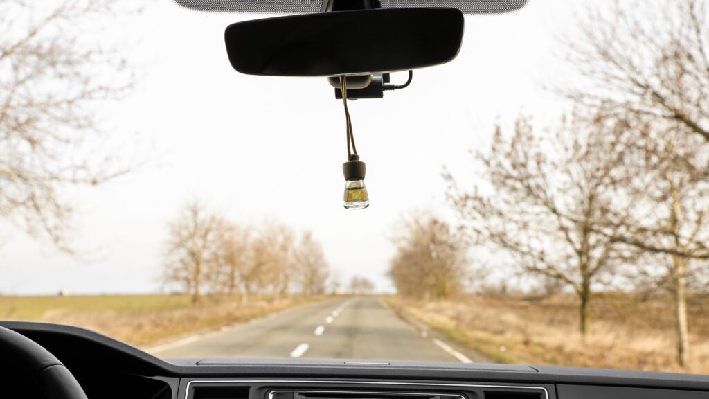 First person view of a rearview mirror with a car freshener hanging off of it.