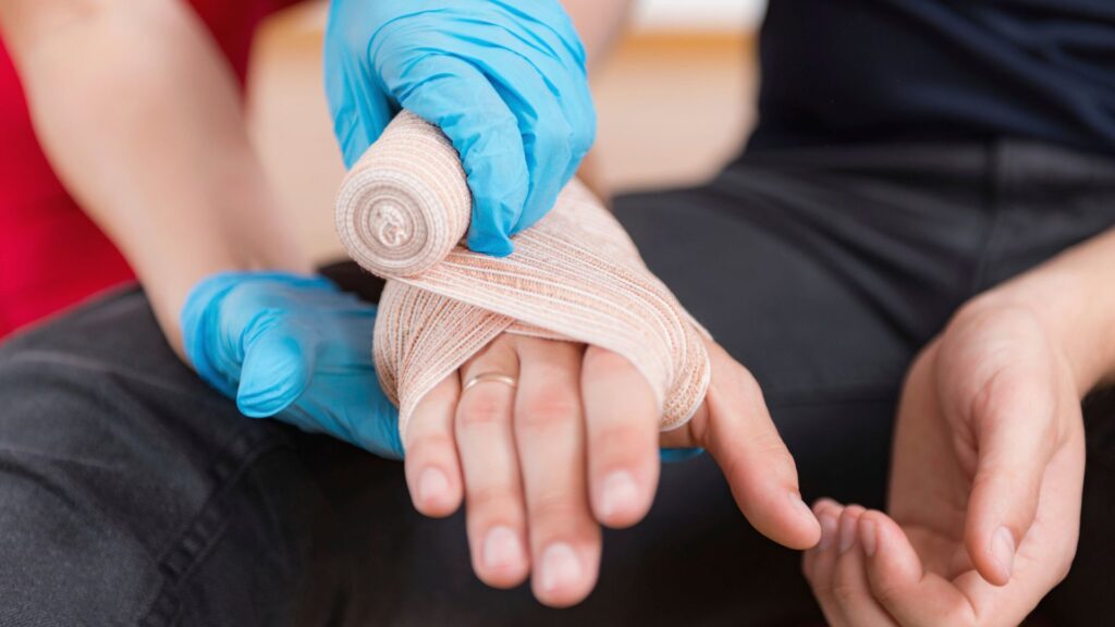 Woman with blue gloves wrapping a bandage around a man's hand.