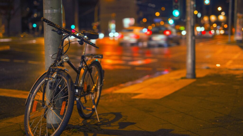 Nighttime view of a bicycle rested upon a street post with cars in the street behind.
