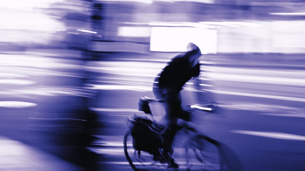 Blurry image of a hooded man riding a bike.