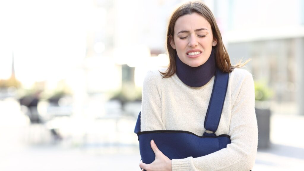 Woman wearing a blue arm sling holding her arm in pain.