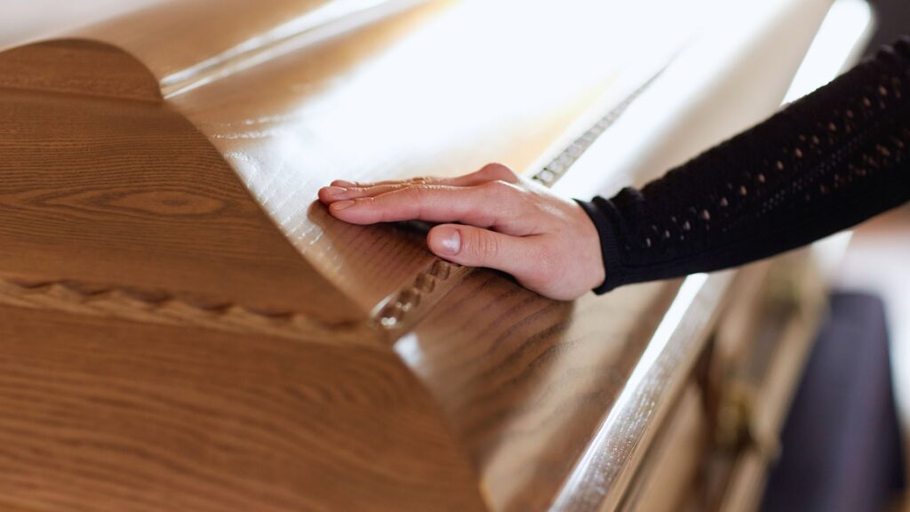 Close-up of a woman's hand laid upon a closed wooden casket.
