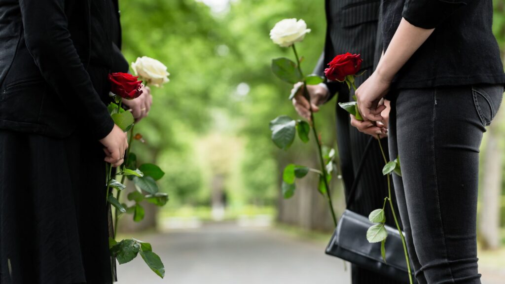 Mourning family wearing black standing facing each other with roses in their hands.